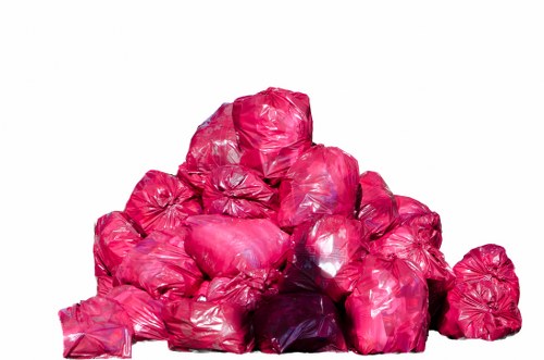 A large pile of tightly compressed black bin bags made of glossy, bright pink plastic material, situated on a smooth white surface with no background scenery visible. The bags are stacked irregularly, with some leaning against others, creating a mound approximately two to three times the height of a typical person. Each bag appears to be filled with waste, evident from their rounded, bulging shape and slightly uneven surface. The bags' shiny finish reflects light, emphasizing their vibrant color, and the pile occupies the foreground, suggesting a waste collection or rubbish removal scene typical of commercial or domestic clearance services. This arrangement demonstrates the type of waste management services provided by companies such as Office Clearance Yiewsley, supporting professional rubbish disposal needs in the local area, including the town of Yiewsley and surrounding regions. The overall composition indicates a tidy, organized collection of waste ready for removal, aligned with the company's focus on rubbish clearance support.