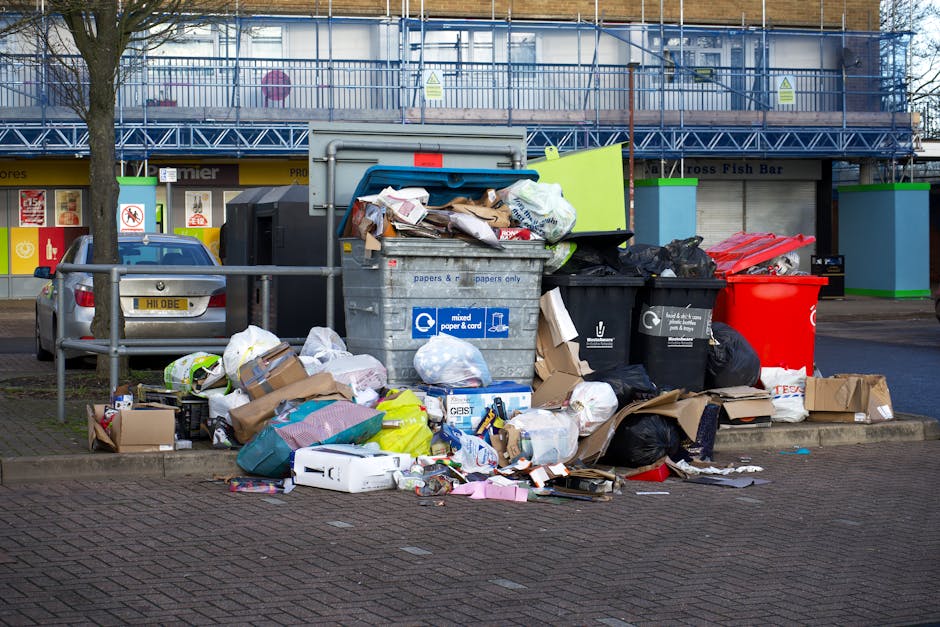 A large outdoor pile of mixed household waste, predominantly consisting of numerous plastic items such as containers, bottles, and caps in various colors including white, blue, green, pink, and red. T